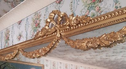 null A large carved and gilded wood mirror with a Louis XVI style floral knot and...