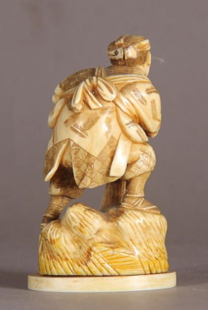null Two ivory okimono, one representing a peasant holding a sword, the other representing...