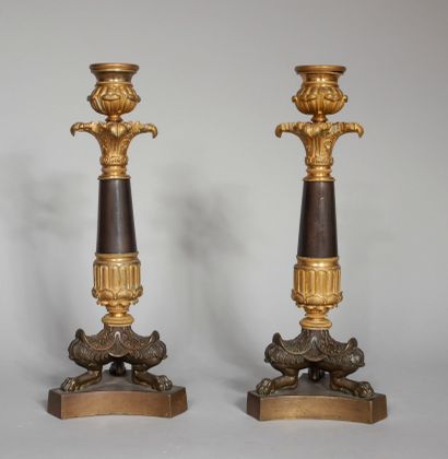 null A pair of patinated and gilt bronze candlesticks resting on three shanks and...