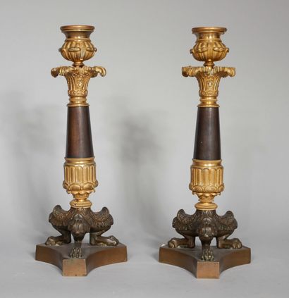 null A pair of patinated and gilt bronze candlesticks resting on three shanks and...
