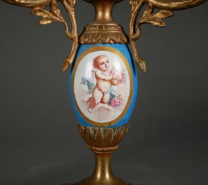 null A pair of bronze and porcelain candelabras decorated with putti and bouquets...