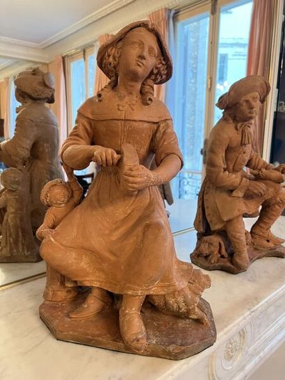 null Two terracotta sculptures depicting a seated young woman cutting a loaf of bread,...