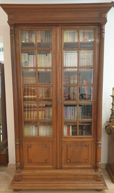 null Bookcase in molded and carved natural wood opening with two glass doors, engaged...