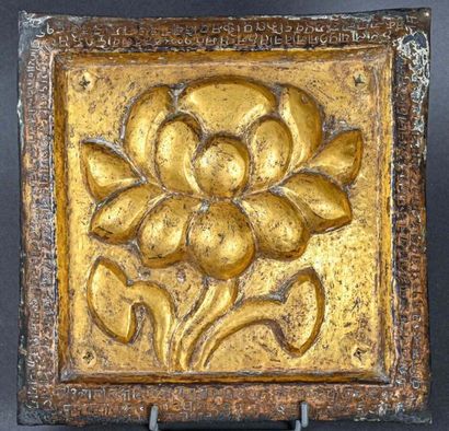 null TIBET - XXe siècle
Plaque carrée en bronze, à décor repoussé et doré d'une fleur...