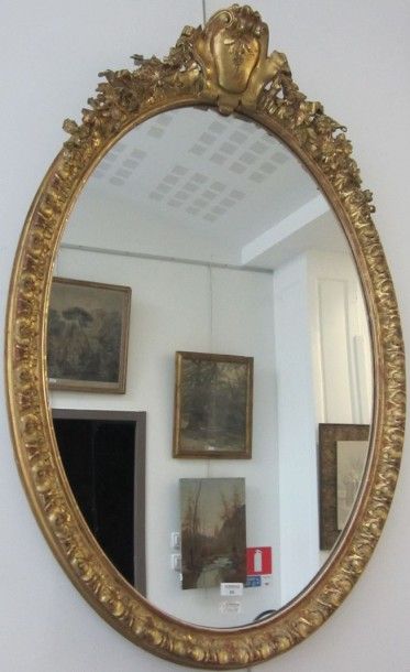 null Miroir ovale en stuc doré orné au fronton d'un cartouche mouvementé et de guirlandes...
