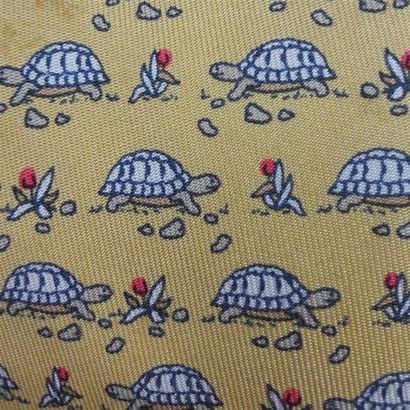 null HERMÈS Paris. Cravate en soie imprimée à motifs de tortue sur fond ocre (tâches)....