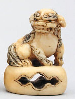 null NETSUKE en ivoire représentant un Shishi sur une base ovale ajourée et un revers...