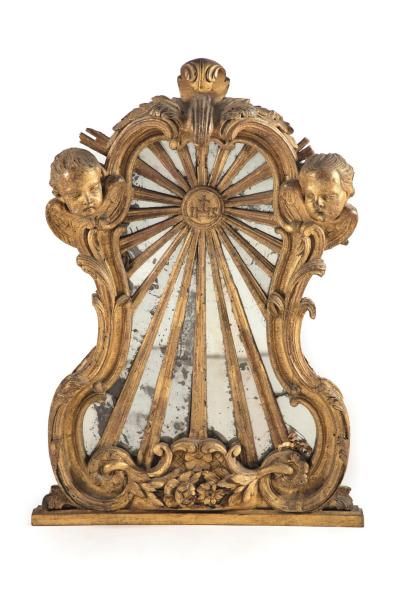 Miroir en bois doré et sculpté à décor rayonant orné de trois têtes d'ange éléments...