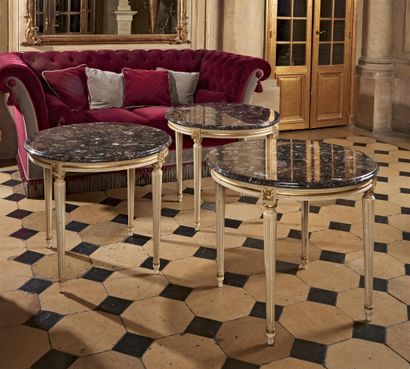 null TROIS PETITES TABLES rondes en bois laqué blanc et or, dessus de marbre gris.
Style...