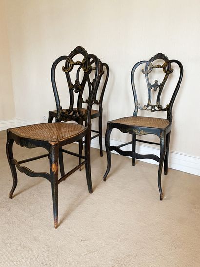 null Suite of three caned chairs In black and gilded wood, decorated with scrolls...