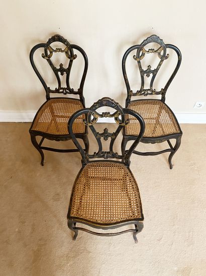 null Suite of three caned chairs In black and gilded wood, decorated with scrolls...