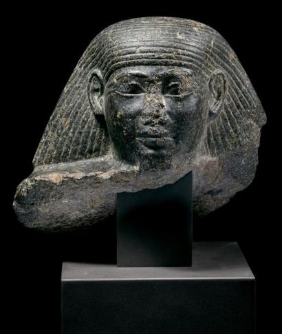 ÉGYPTE TÊTE MASCULINE DE STATUE-CUBE. Le dignitaire est coiffé d'une perruque évasée,...