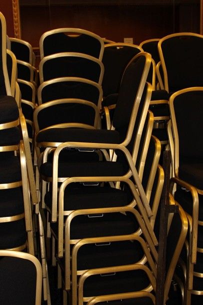  Suite de cent chaises empilables en métal doré, assise et dossier garnis de tissu...