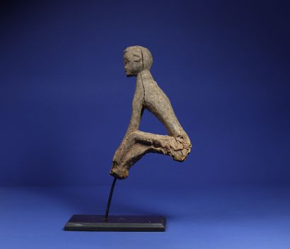 null 
Top of a divination stick showing a seated figure, arms joining the legs bent...