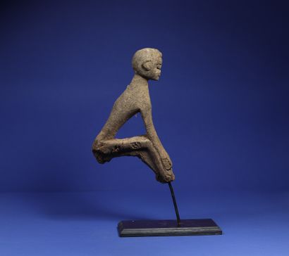 null 
Top of a divination stick showing a seated figure, arms joining the legs bent...