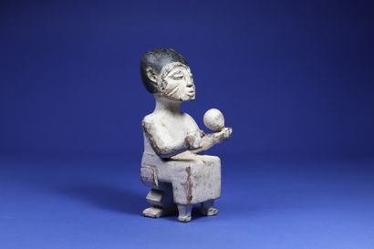  Person seated on a stool, holding a spherical object in his left hand and another...