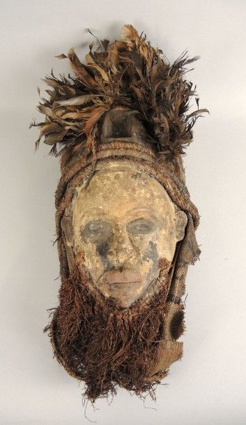 ART AFRICAIN Masque en bois peint d'argile. Contex en fibre végétale, coiffe en plumes....