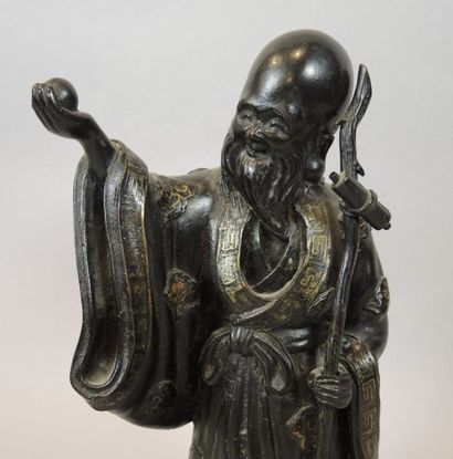 CHINE Statuette en bronze à patine noire et rehaut or représentant un sage tenant...