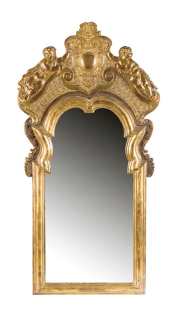 null A gilt brass mirror on a wooden core, with a rich decoration of cherubs, cartouches,...