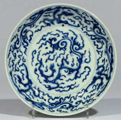 CHINE Assiette en porcelaine bleu et blanc à décor de dragons et de nuages stylisés....