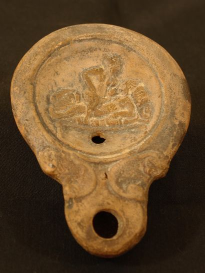 null Terracotta oil lamp with round spout framed by volutes with erotic decoration....