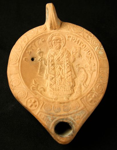 null Oil lamp in beige terracotta decorated with a nimbed saint holding a Bible on...