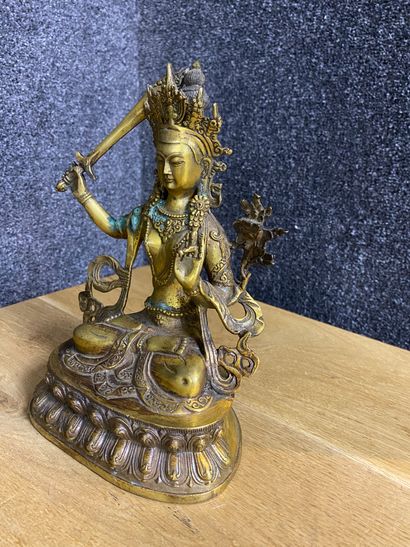 null 
Bouddha en bronze doré assis en position de méditation, la main droite tenant...