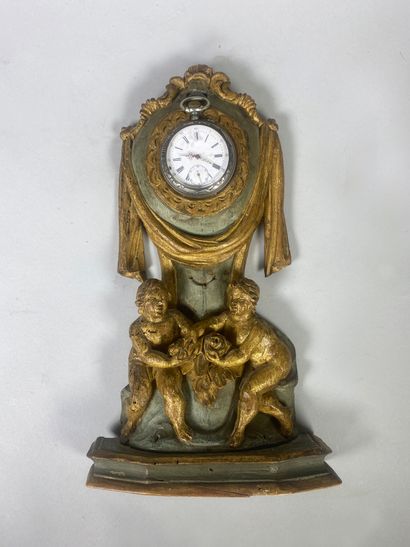 null A grey-blue and gilded painted wood watch stand carved with two putti on the...