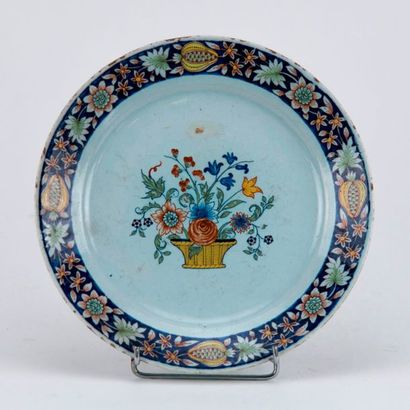 ROUEN Assiette en faïence à décor polychrome au centre d'un panier fleurie. Sur l'aile,...