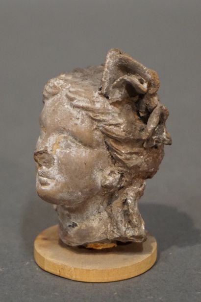 null Female head with hair held by a thick plant crown. Ochre terracotta. Crown partly...