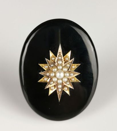  Broche ovale en onyx à décor d'une étoile en or jaune ornée de petites perles. 
L'intérieur...