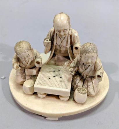 null Well carved ivory group of a kneeling man explaining the game of GO to two children...