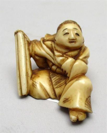 null Netsuke en ivoire bien sculpté et à belle patine d’un enfant assis, un sac de...
