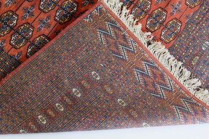 PAKISTAN Grand tapis de style Boukhara, champ brun-rouge orné de göls polychromes,...