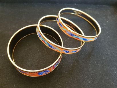 HERMES 3 bracelets joncs en métal doré émaillés à décor de plumes sur fond orange....