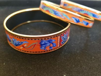 HERMES 3 bracelets joncs en métal doré émaillés à décor de plumes sur fond orange....