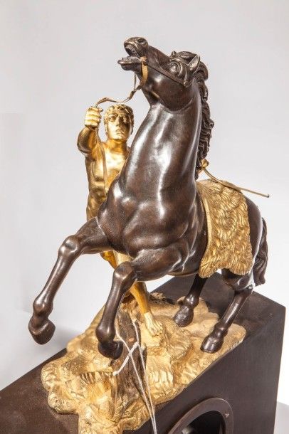 null Pendule en bronze doré et bronze patiné- Surmontée d'un "cheval de Marly". Le...