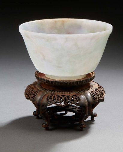 CHINE A light grey carved jade bowl with green spots. Presented on a carved wooden...
