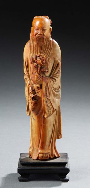 CHINE Figurine en ivoire à patine brune représentant un immortel tenant une fleur...