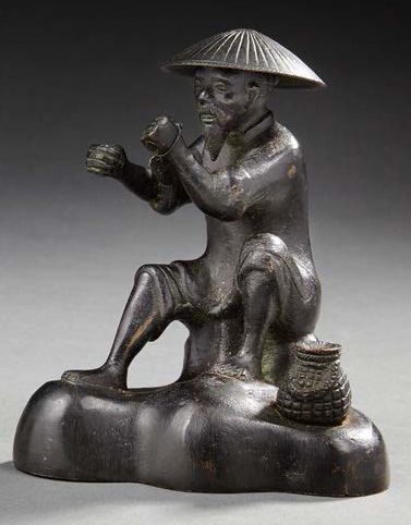 JAPON Figurine en bronze représentant un pêcheur assis sur un rocher, une nasse près...