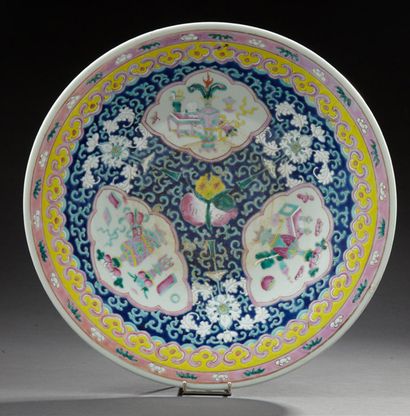 CHINE Plat circulaire en porcelaine décoré en émaux de la famille rose d'objets precieux.
Premier...