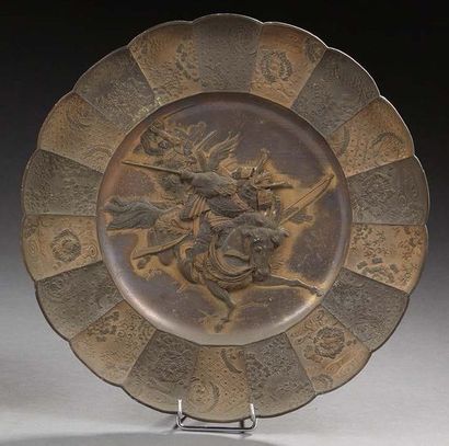JAPON Plat en bronze à patine brune et or décoré au centre en léger relief du combat...