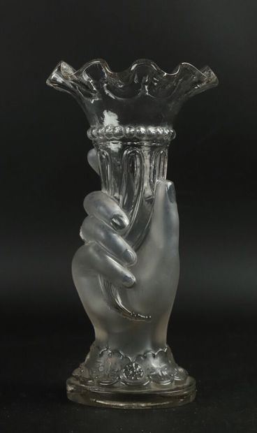 Vase en verre moulé tenu par une main. 
Vers...