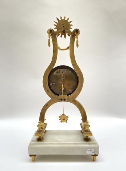 null Lyre clock in gilt bronze underlined by friezes of pearls, surmounted by a radiant...