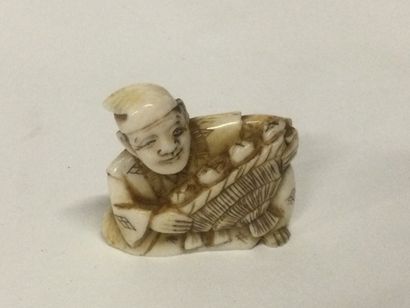null JAPAN. A carved ivory netsuke with a figure holding a basket, signature on the...