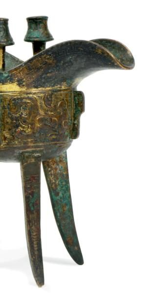 CHINE - XVIIe siècle Verseuse tripode "jue" en bronze doré, à décor incisé de masques...