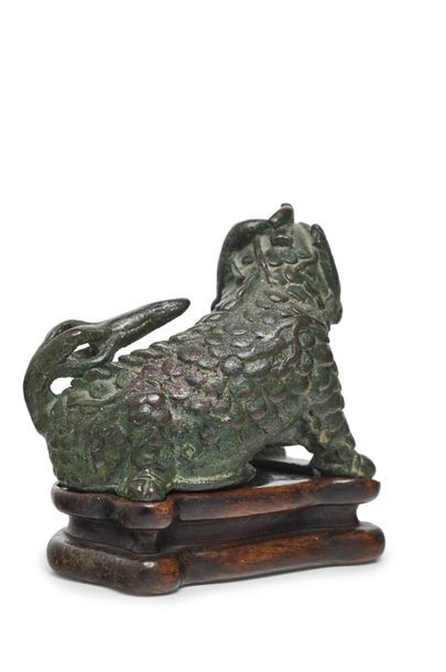 CHINE Statuette de qilin en bronze à patine verte assise, la tête tournée légèrement...