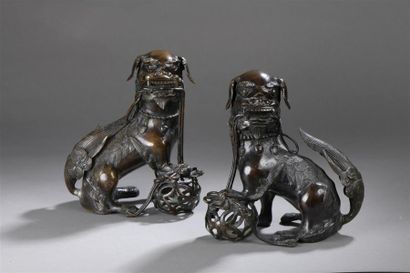  Deux chiens de Fô assis à la boule en bronze à patine brune formant paire. Indochine,...