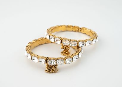 CHANEL Deux bracelets joncs en métal doré ornés de strass blancs. 
Ouverture à charnière....