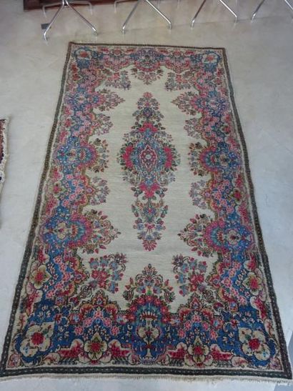 KIRMAN 

Tapis en laine à fond beige à décor au centre d'un médaillon et de frises...